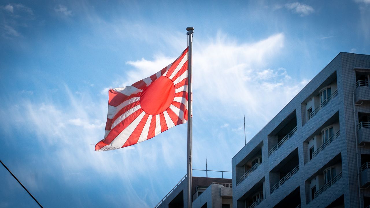 The Rising Sun flag flying against a blue sky beside an apartment block.