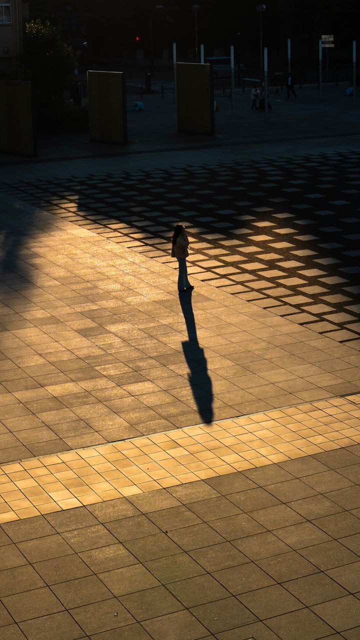 A lone person casting a long shadow across sunlit paving at golden hour.