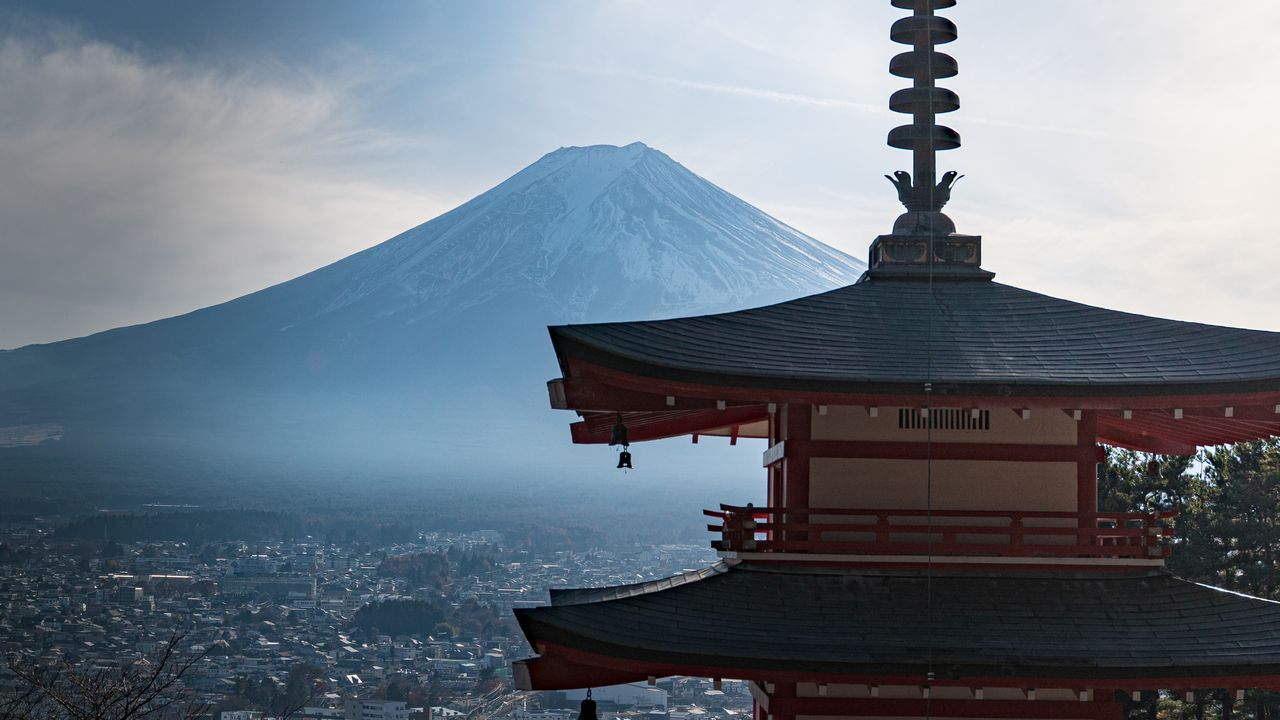 A red pagoda in the foreground, with snow-capped Mount Fuji and a town below.