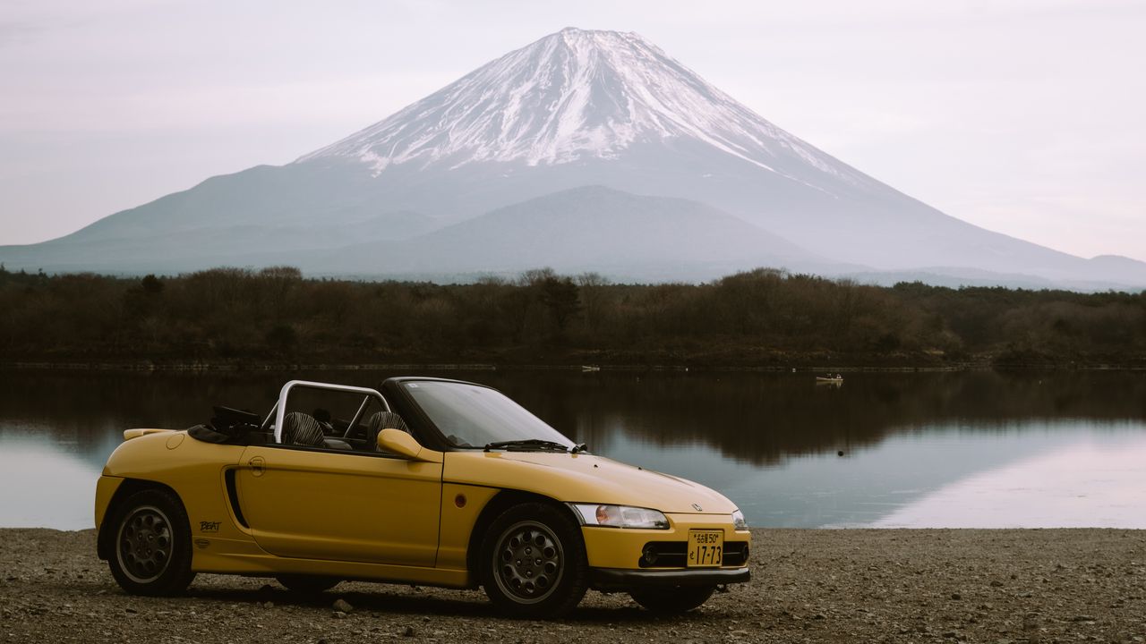A yellow convertible parked on a lakeshore with Mount Fuji behind.