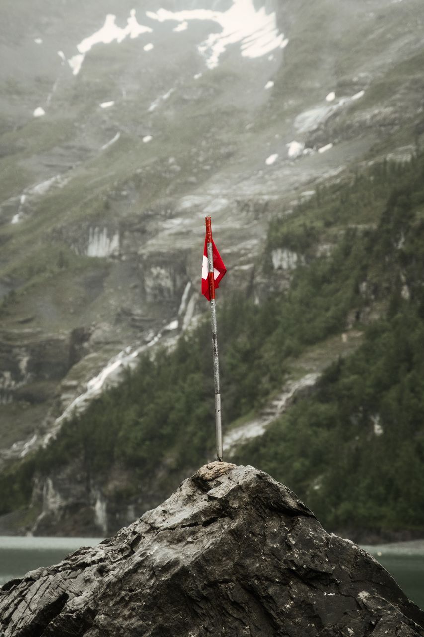A small Swiss flag on a pole planted in a rock, misty cliffs behind.