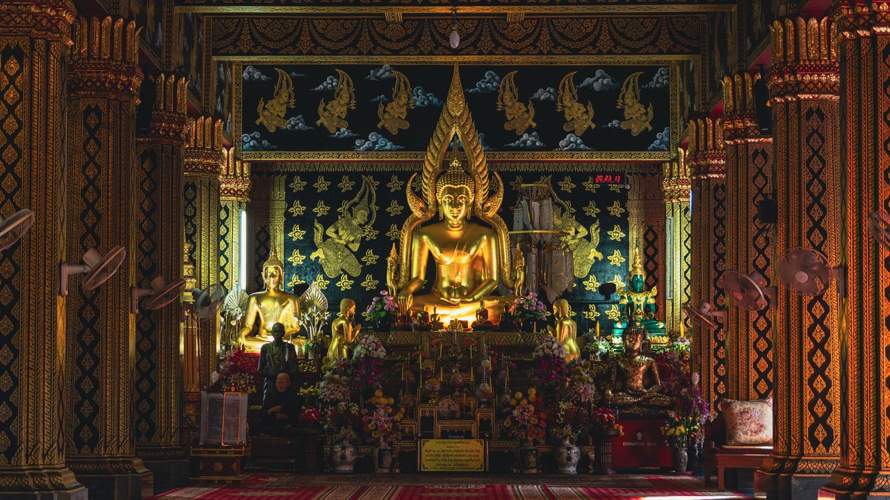A golden seated Buddha in a temple hall lined with black-and-gold patterned pillars.