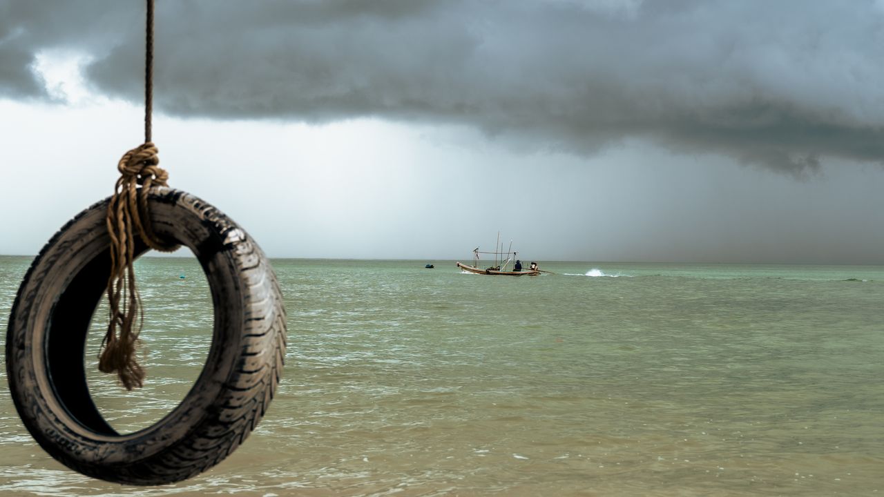 A tyre swing over a green sea as a longtail boat heads out under a storm.